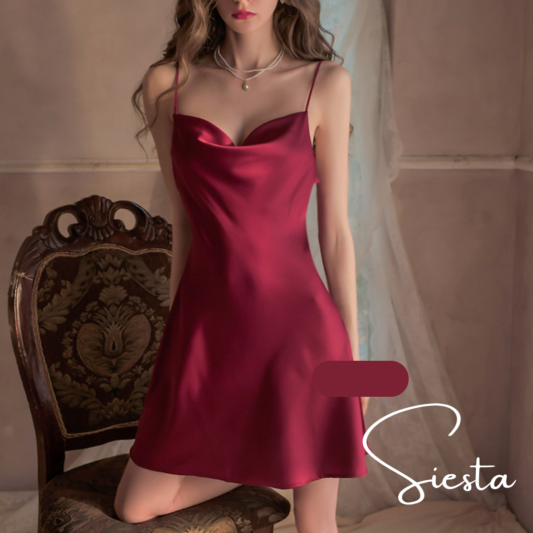 Woman wearing a red satin slip dress in a softly lit room with 'Siesta' branding.